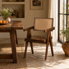 Lifestyle image of an acacia wood chair with rattan backrest and armrests; elegant wooden armchair for dining or living rooms, 55 × 55 × 85 cm.