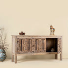 Open door view of a console table made from old teak door panels, featuring traditional hand-carved details, iron ring accents, and built-in storage in a natural rustic finish.