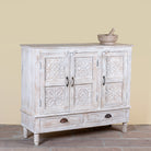 Side angle image of a whitewashed hand carved wooden sideboard made from solid mango wood with floral patterns, 3 doors and 2 drawers; artisanal mango wood furniture, 120 × 100 × 40 cm.