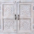 Close up image of a whitewashed hand carved wooden sideboard made from solid mango wood with floral patterns, 3 doors and 2 drawers; artisanal mango wood furniture, 120 × 100 × 40 cm.