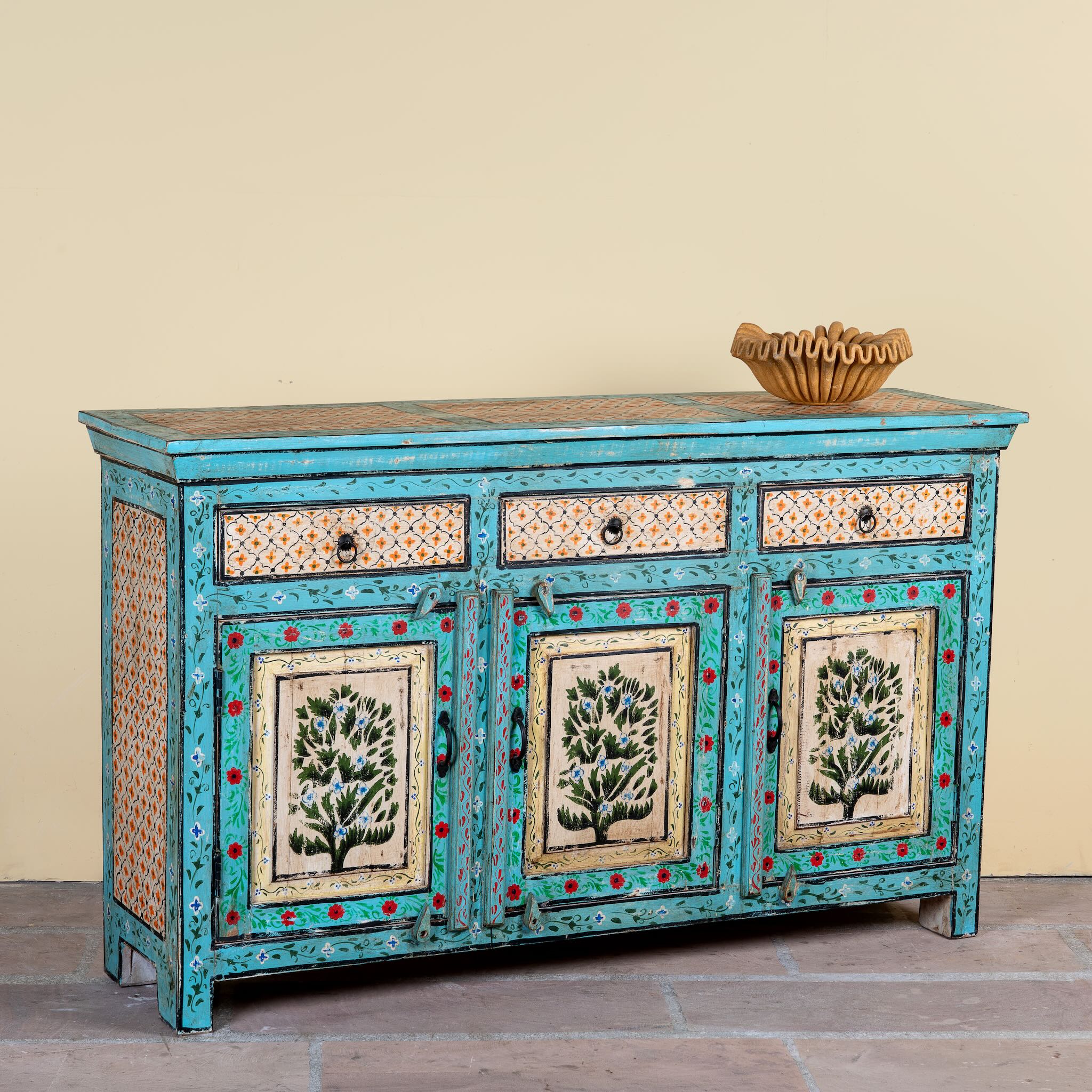 Side angle image of a Kaveh hand painted reclaimed wood sideboard in boho style with three doors, three drawers, floral details, and distressed turquoise finish.