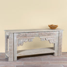 Side angle image of a Kayleb reclaimed teak console table with hand-carved Indian floral details, lower shelf, and whitewashed vintage finish.