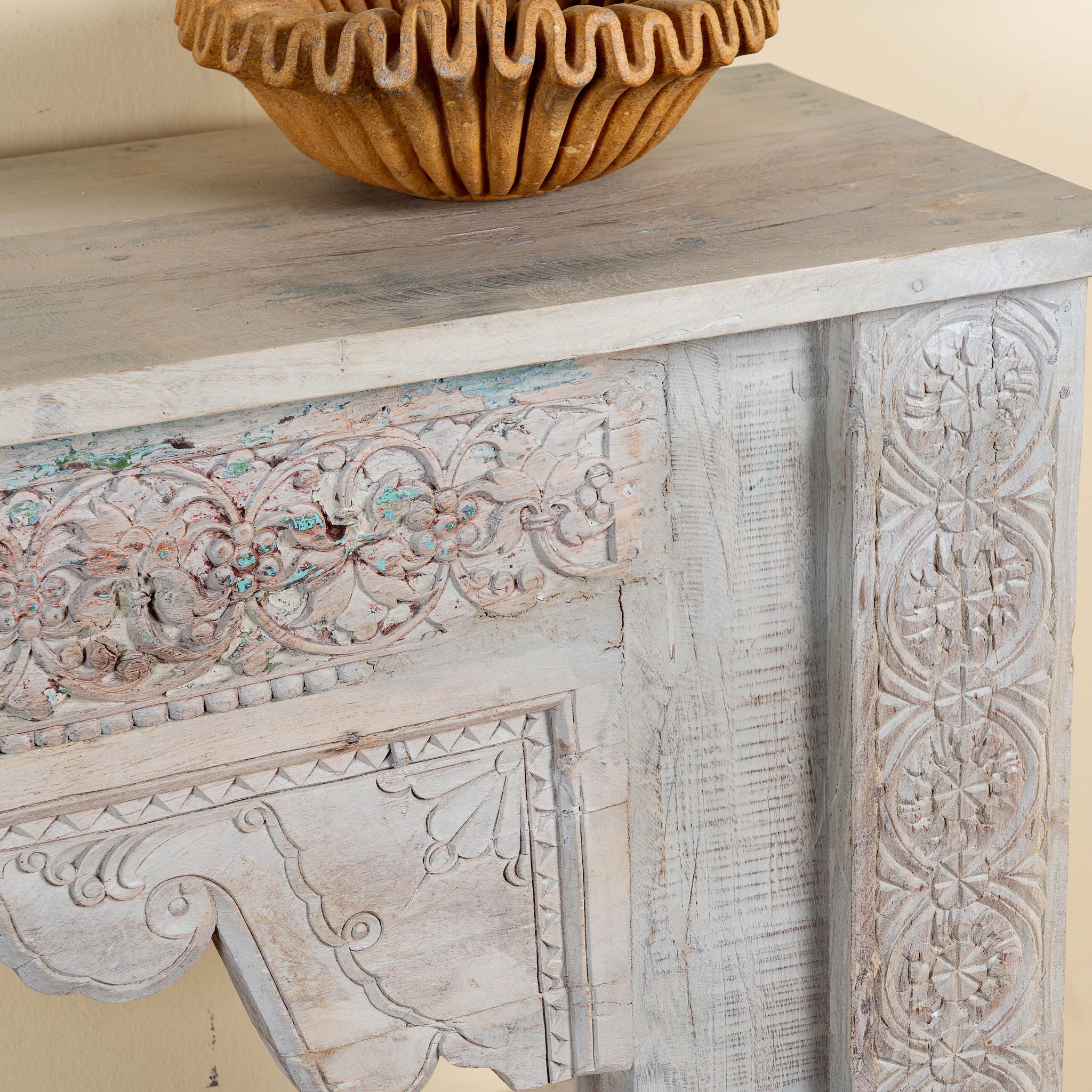 Close up image of a Kayleb reclaimed teak console table with hand-carved Indian floral details, lower shelf, and whitewashed vintage finish.