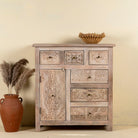 Front view of a hand carved mango wood cupboard with 6 drawers and 1 door, iron fitted door knobs and floral carvings.