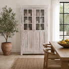 Lifestyle image of a refurbished antique teak wood display cabinet with whitewashed finish and glass doors – wooden display cabinet blending Mediterranean charm and timeless craftsmanship.