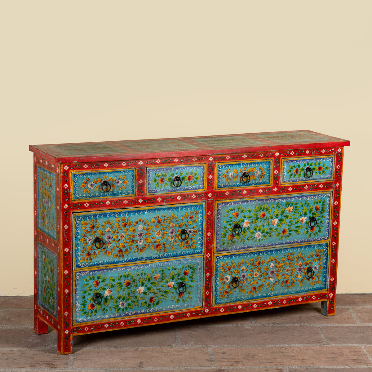 Side angle image of a Kianraj hand painted reclaimed wood chest of drawers with red frame, blue floral fronts and eight drawers 150cm