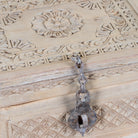 A rustic, antique-style metal latch with a chain lock resting on a carved wooden box lid.