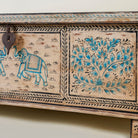 Side view close up image of a large hand-painted chest made from old reclaimed wood, featuring intricate blue designs of elephants and floral motifs on a distressed beige background, with a central latch and a rustic vintage finish.
