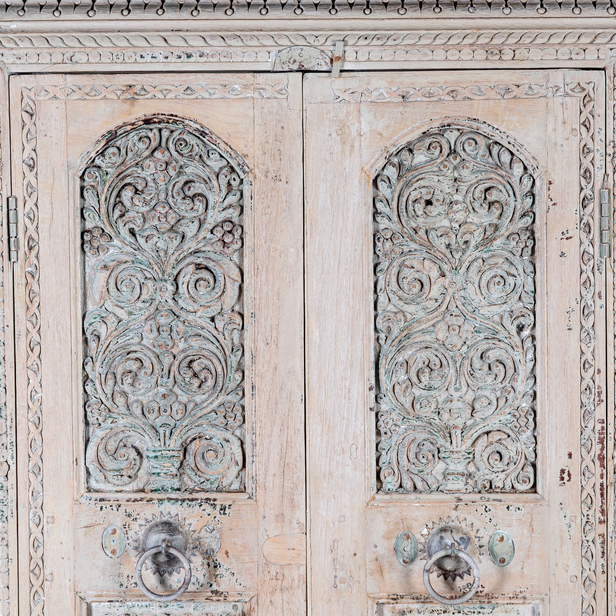 Close up image of a Kyra antique reclaimed teak wood wardrobe with intricate Indian hand carvings, double doors, and vintage distressed finish.