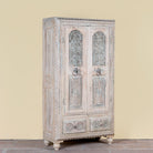 Side angle image of a Kyra antique reclaimed teak wood wardrobe with intricate Indian hand carvings, double doors, and vintage distressed finish.