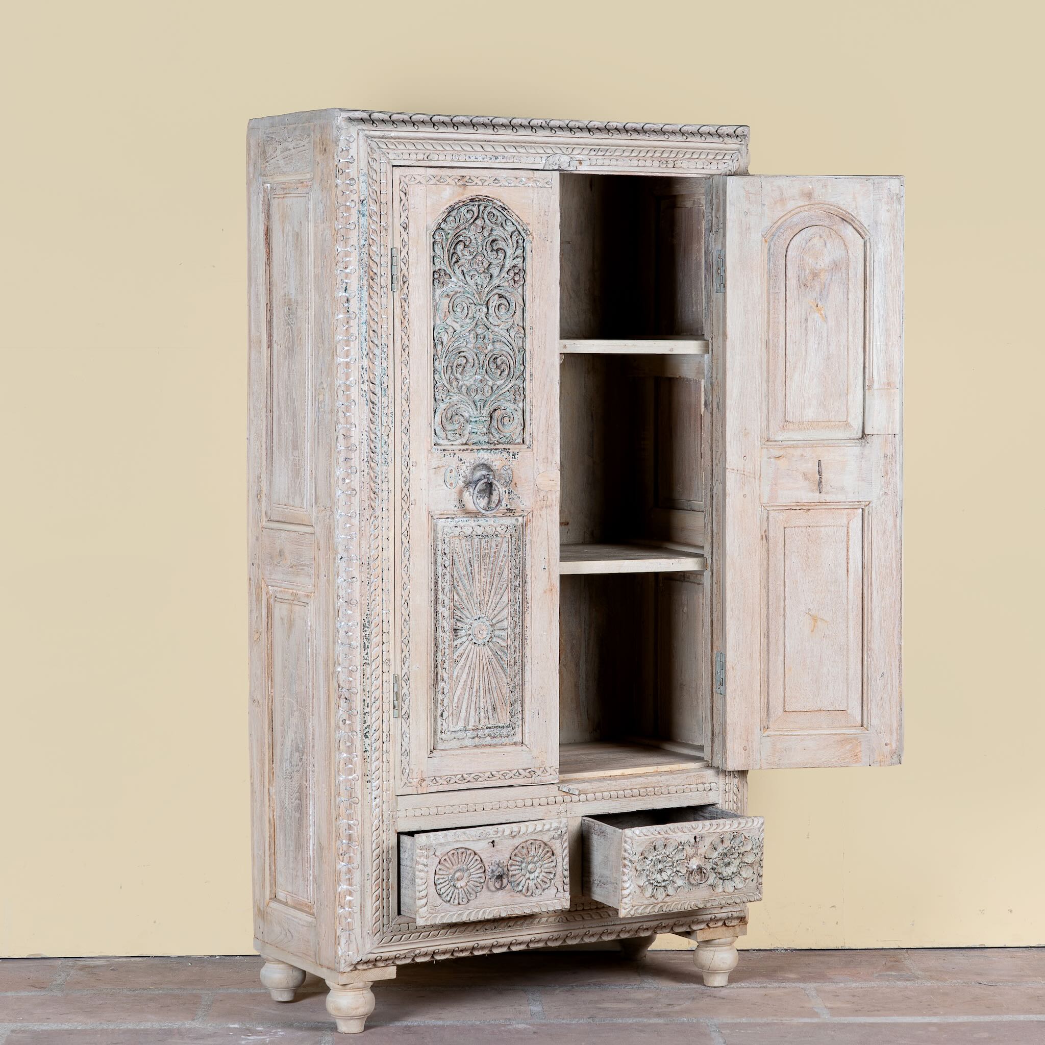 Side angle image with open doors of a Kyra antique reclaimed teak wood wardrobe with intricate Indian hand carvings, double doors, and vintage distressed finish.