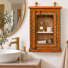 Lifestyle image of a Lokesh hand-painted reclaimed wood wall cabinet with orange floral decoration, turquoise accents, glass door and interior shelf, 40x15x52cm
