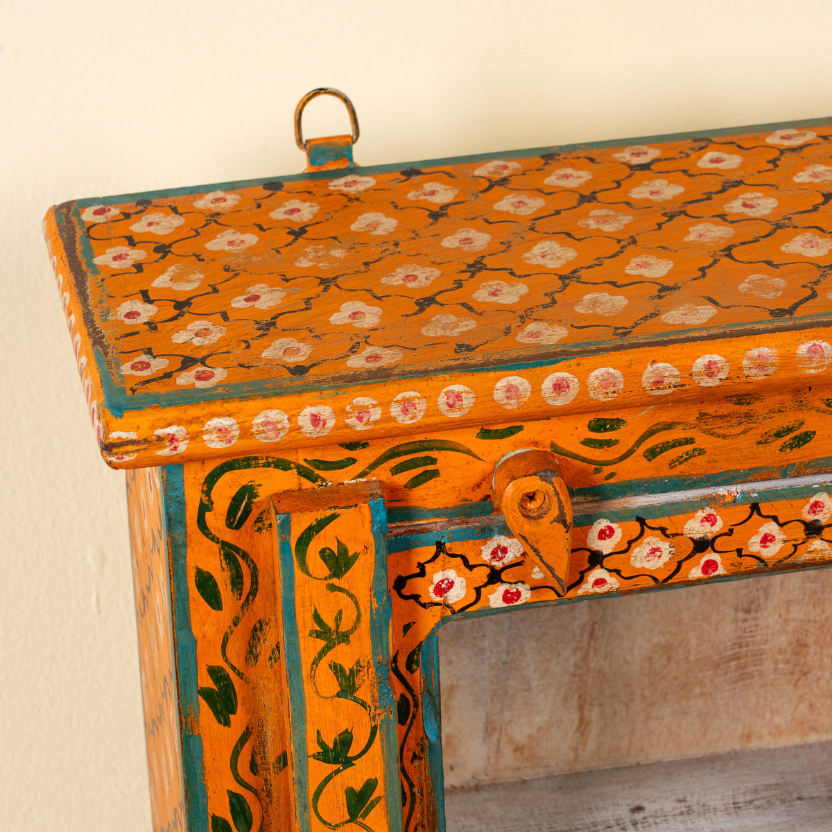 Close up image of a Lokesh hand-painted reclaimed wood wall cabinet with orange floral decoration, turquoise accents, glass door and interior shelf, 40x15x52cm