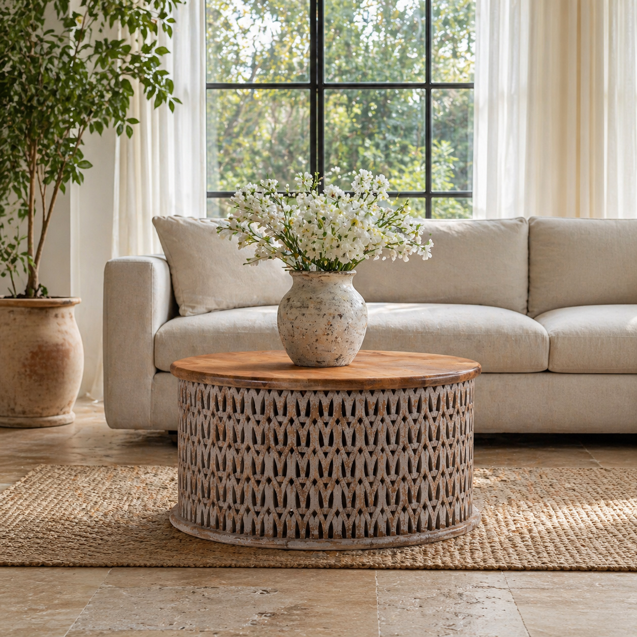 Lifestyle image of a round hand carved mango wood coffee table with white-washed base and natural wood top; 90 cm diameter, 45 cm height.