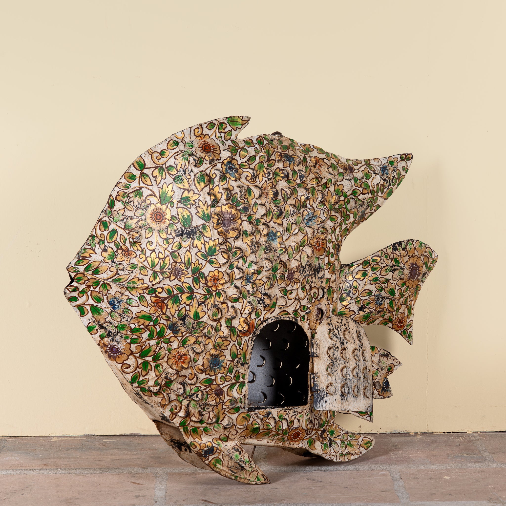 Side angle image of a Malini hand painted freestanding metal fish sculpture with intricate floral artwork in soft green, cream and earthy tones, handcrafted decorative home accessory, 107x15x80cm.