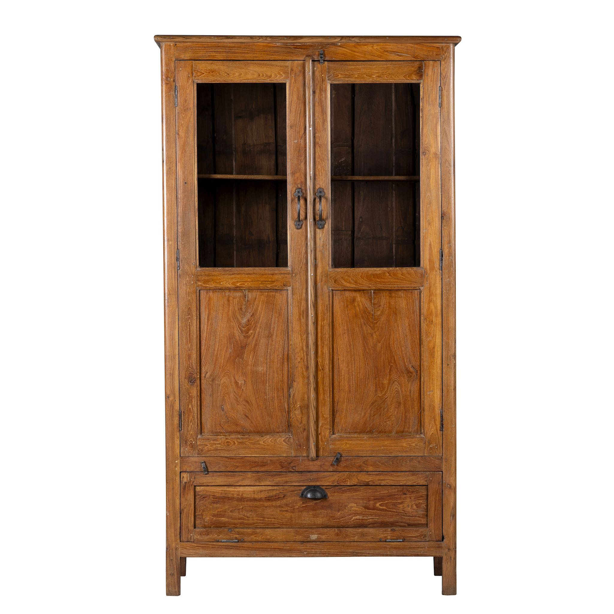White background image of a tall reclaimed teak wood display cabinet with two glass doors and a bottom drawer – wooden display cabinet crafted as sustainable furniture with natural elegance.