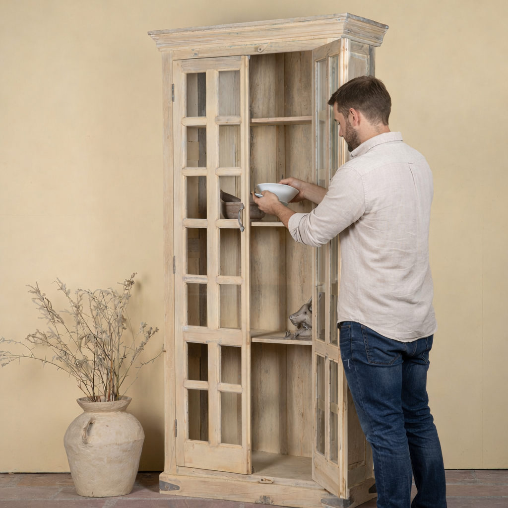 Side angle image with open door of a reclaimed wood display cabinet Eknoor with glass-panelled doors and natural weathered finish. Sustainable living room furniture that can also function as a reclaimed wood wardrobe with spacious shelving.
