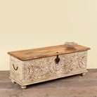 Side angle image of a Hand-carved mango wood chest box with floral motifs, whitewashed finish, and iron handles – vintage home accessory for rustic and elegant interiors.
