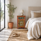 Lifestyle scene of a hand painted bedside table with floral motifs; sustainable furniture made of recycled wood, 45 × 35 × 70 cm.