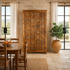 Lifestyle image of a hand-carved mango wood wardrobe with floral motifs; wooden wardrobe in natural finish, 100 × 45 × 190 cm.