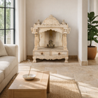 Lifestyle image of a decorative Indian altar made of mango wood, hand carved with 2 small drawers in a living room with a couch and coffee table.