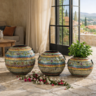 Three decorative vases with floral patterns on a stone patio with flowers and a view of a scenic landscape.