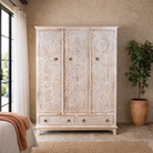 Lifestyle image of a hand carved creme colour mango wood wardrobe wit 2 drawers and 4 shelfs and ample storage.