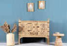 An antique Indian treasure chest in Ibiza style, made of teak wood with intricate hand-carved patterns and iron applications, displayed with decorative items and a vase in the background.