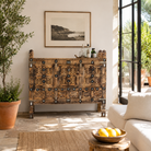 Lifestyle image of an antique Indian treasure chest in solid teak with sandblasted finish, hand-carved details, and iron accents. Vintage home accessory for eclectic Indian decor, 127 × 110 × 47 cm.