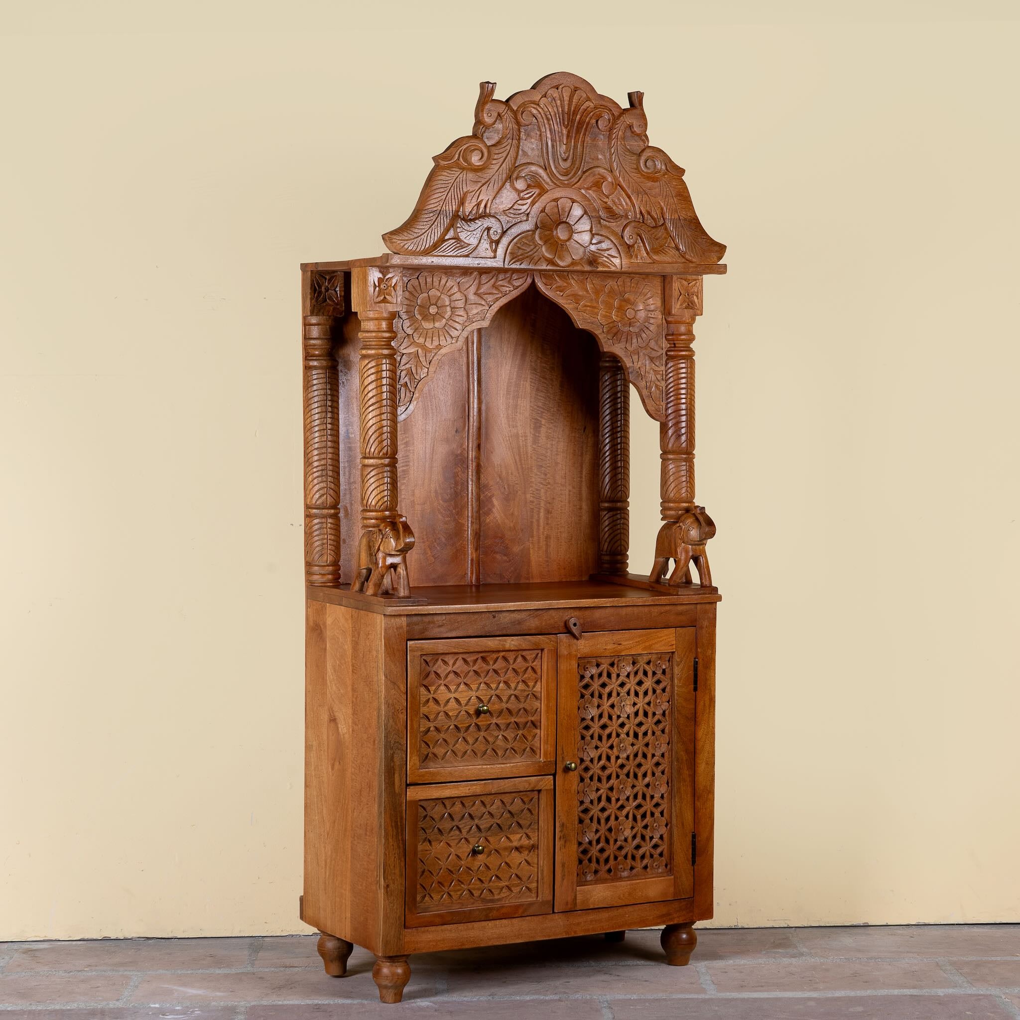 Side angle image of a Moksha hand carved mango wood mandir with decorative Indian carvings, drawers, and cabinet storage.