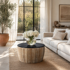 Lifestyle image of a elegant round hand carved coffee table made of sustainable Mango wood with floral design and black marble top.