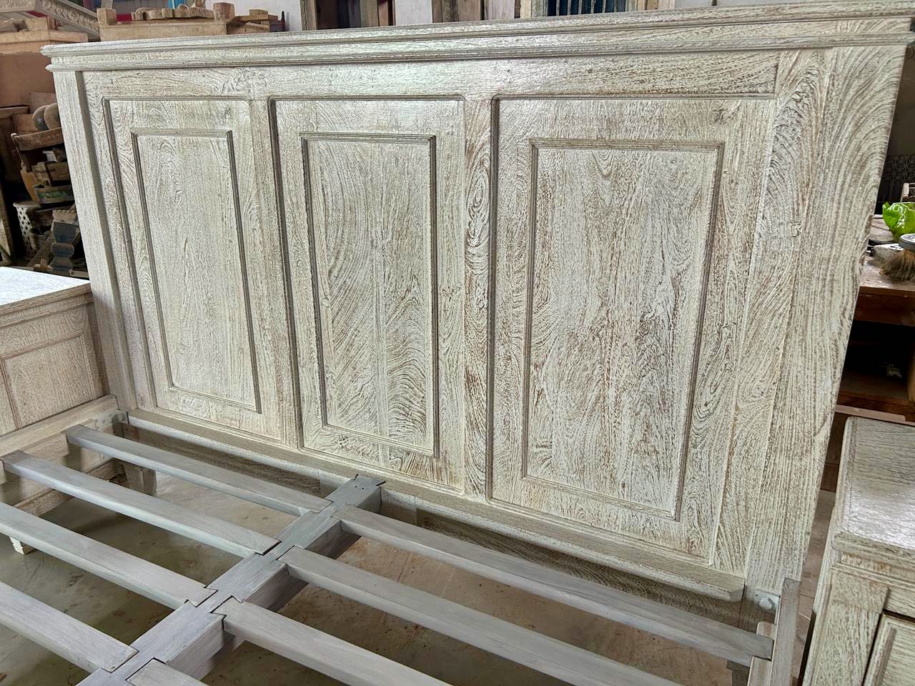 Close up of the headboard of a whitewashed mango wood bed frame with carved panel design and two matching nightstands; rustic bedroom furniture set, bed size 180×200×140 cm, nightstands 50×40×65 cm.