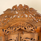 Close up image of a hand carved mango wood Indian mandir temple with ornate floral carvings, lattice doors, and two storage drawers.