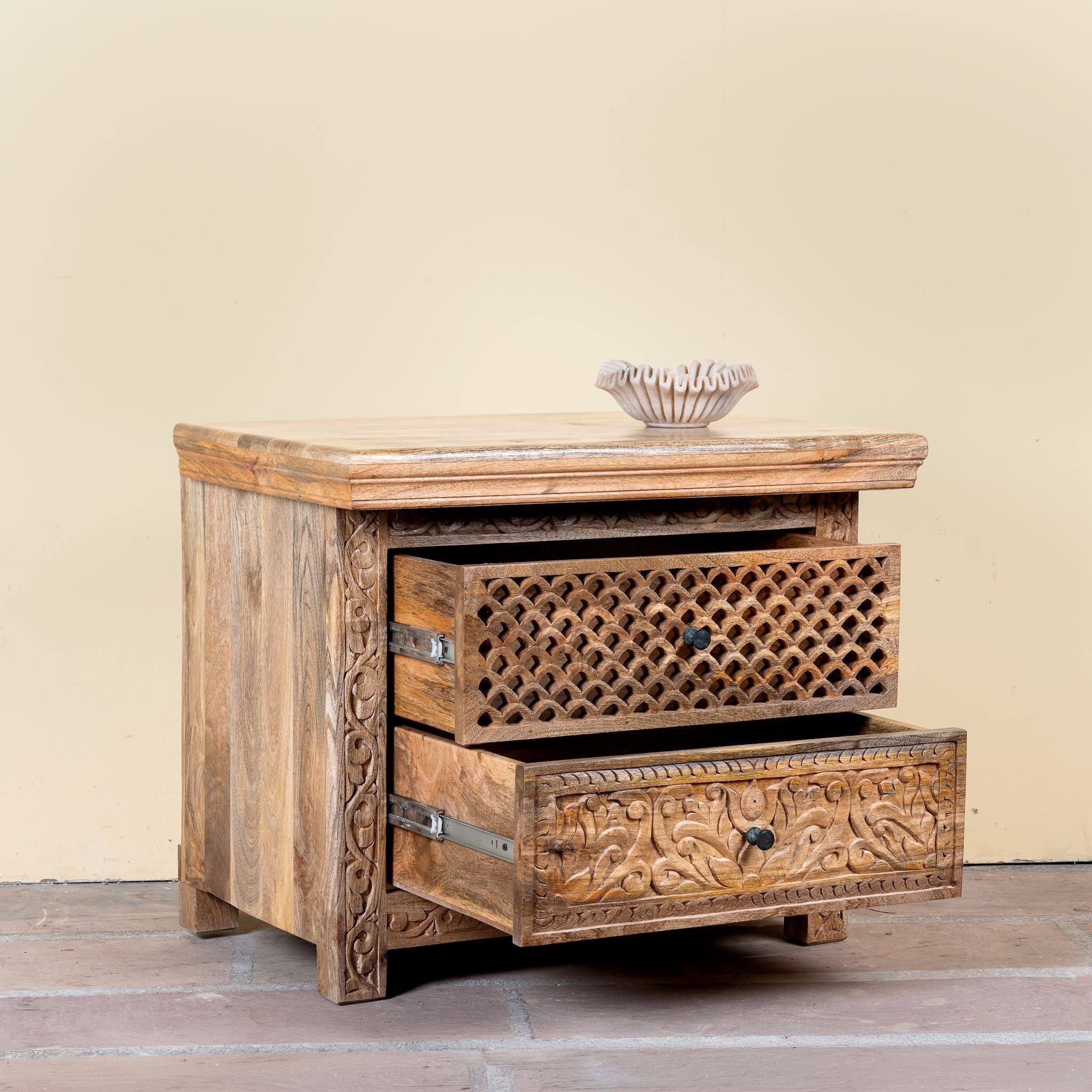 Side angle image with open drawer of a hand carved mango wood nightstand with two drawers and hidden compartment in rustic artisan style.
