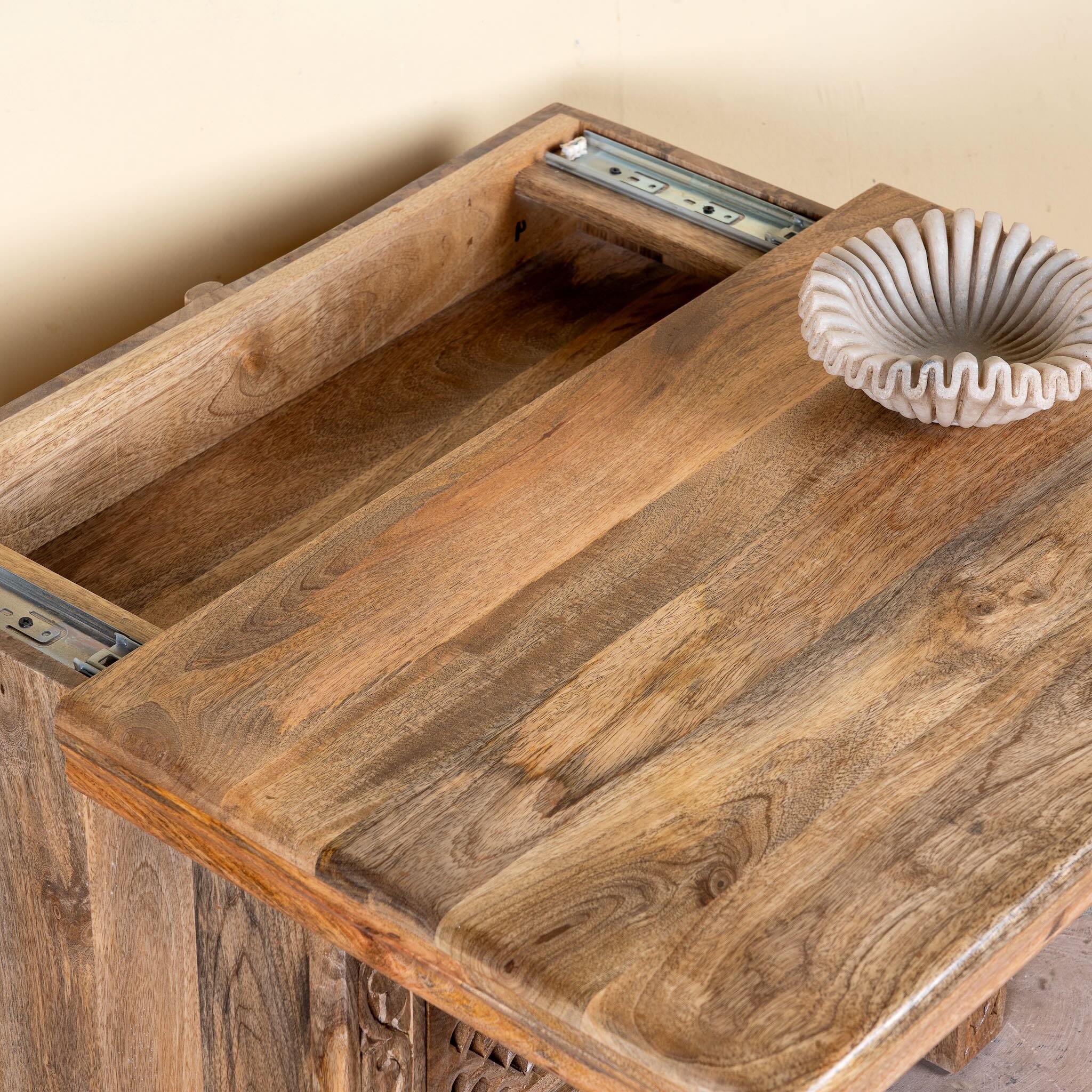 Close up image of a hand carved mango wood nightstand with two drawers and hidden compartment in rustic artisan style.