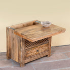 Side angle image showing open lid of a hand carved mango wood nightstand with two drawers and hidden compartment in rustic artisan style.