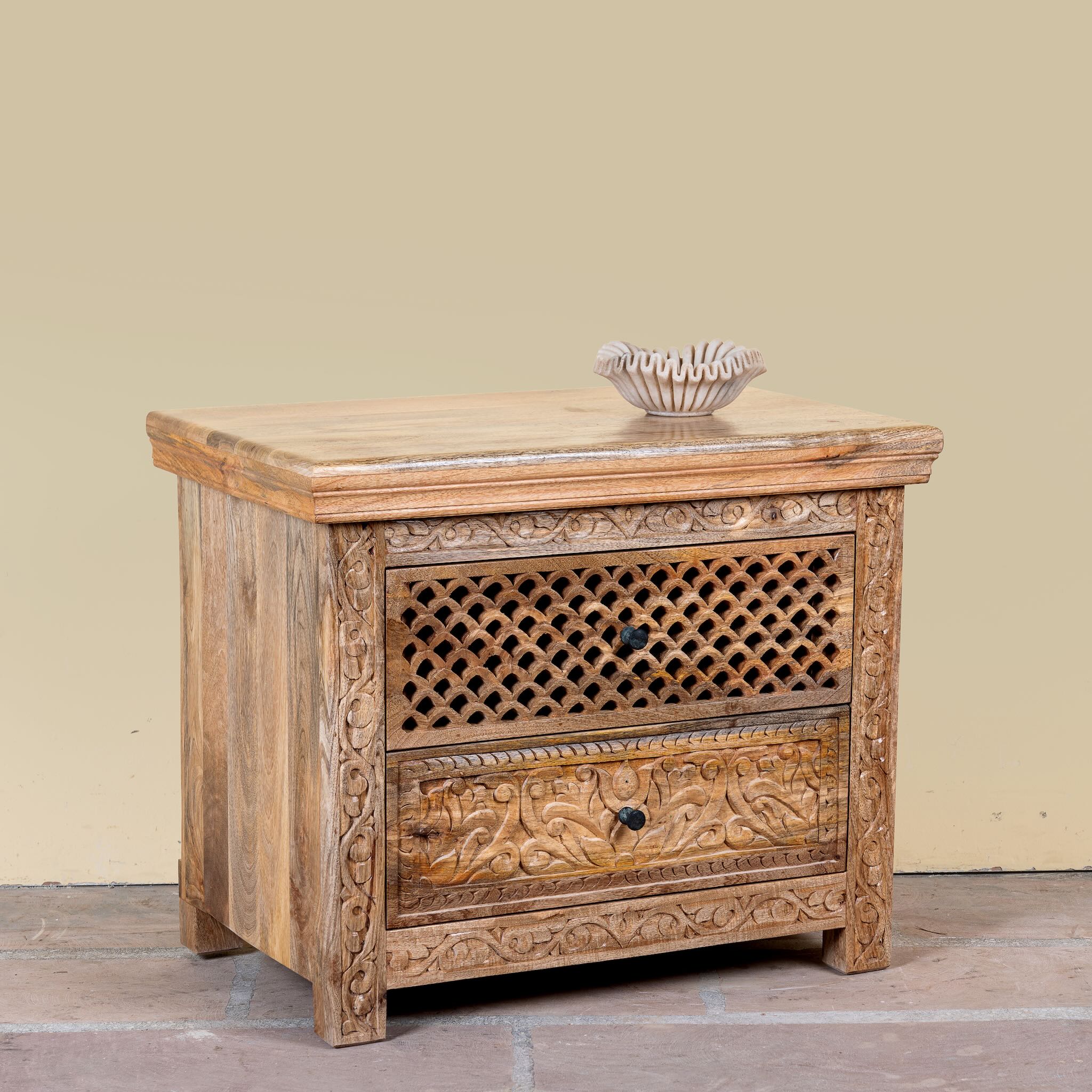 Side angle image of a hand carved mango wood nightstand with two drawers and hidden compartment in rustic artisan style.