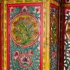 Close up image of a hand carved and hand painted mango wood room divider with colourful floral Indian motifs and folding panels.
