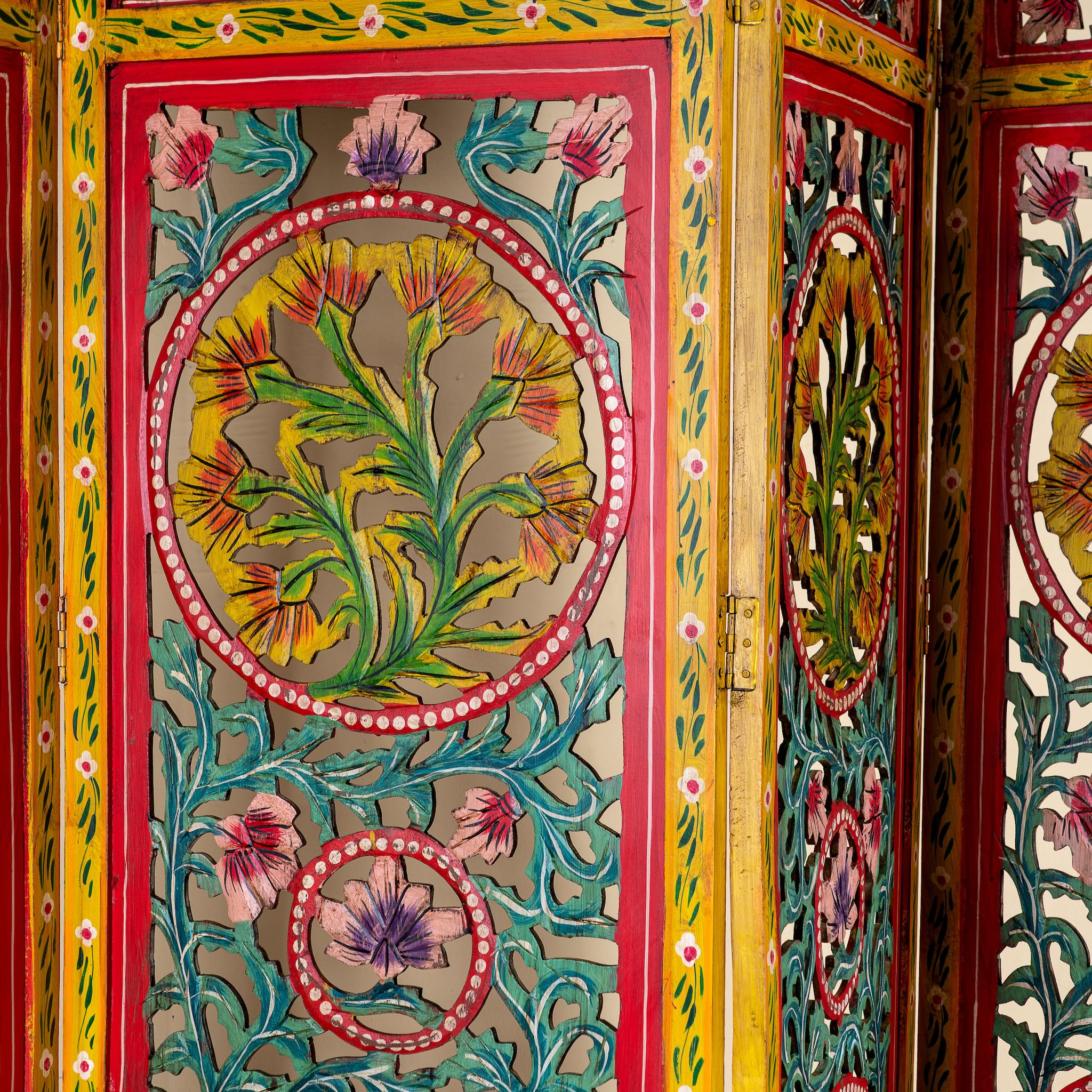 Close up image of a hand carved and hand painted mango wood room divider with colourful floral Indian motifs and folding panels.