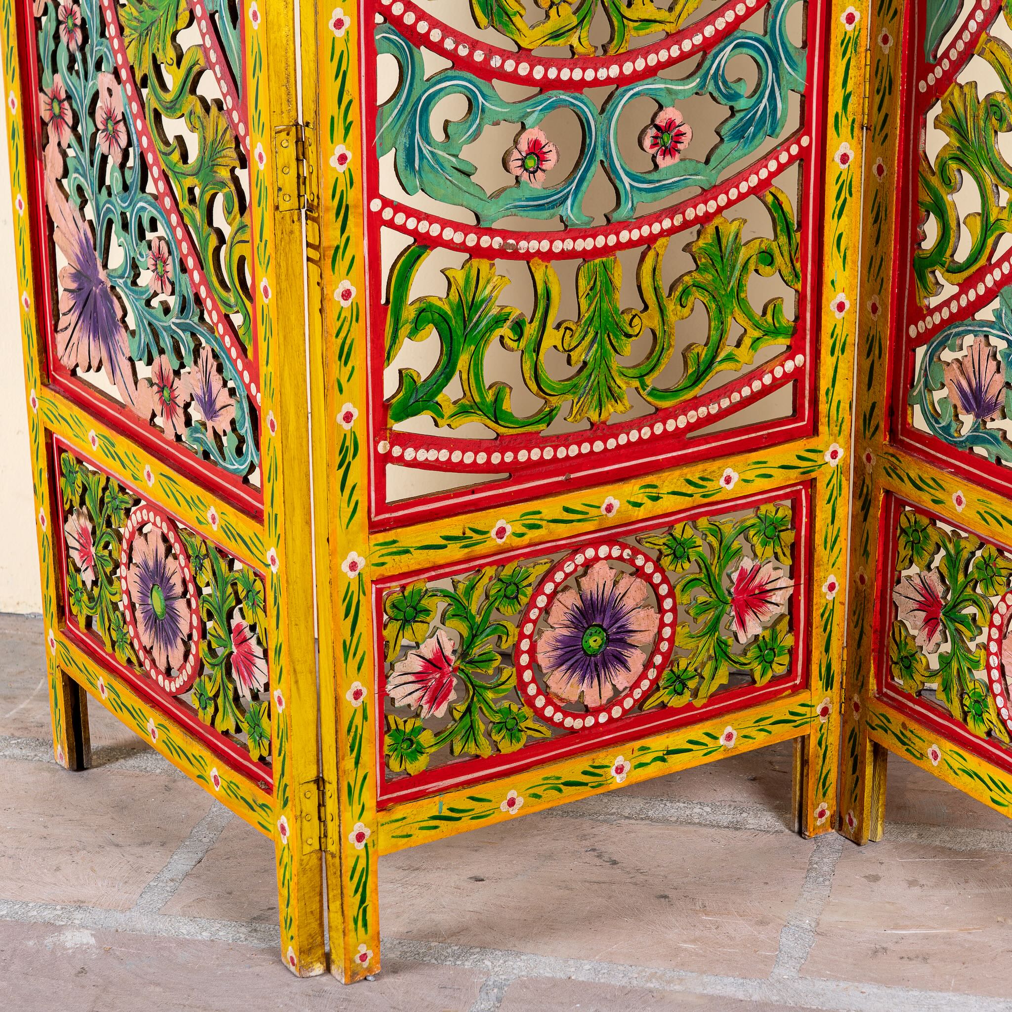 Close up image of a hand carved and hand painted mango wood room divider with colourful floral Indian motifs and folding panels.