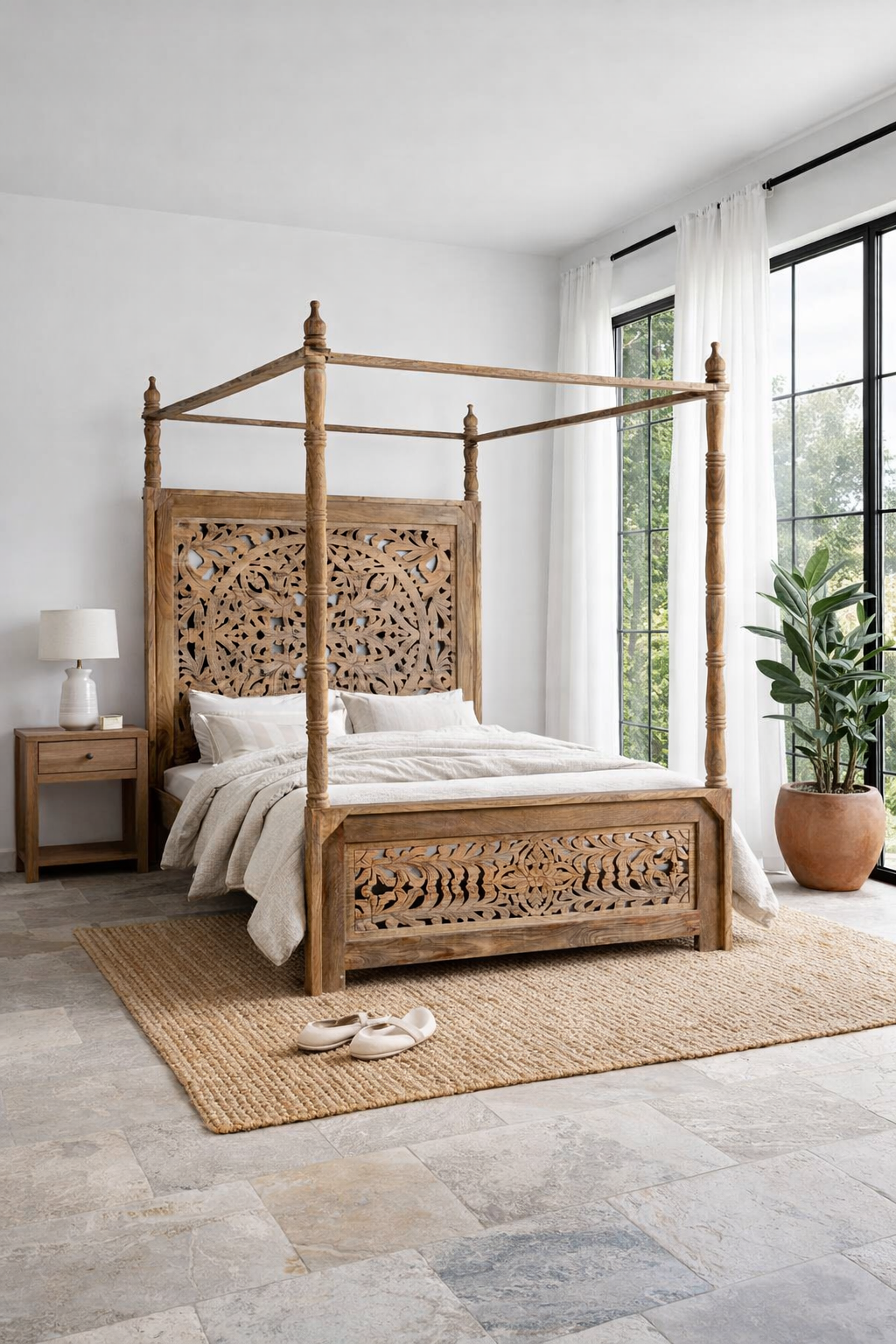 Lifestyle image of a wooden canopy bed with carved headboard in a bedroom with a plant and open door