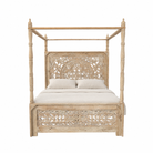 White background image of a wooden canopy bed Nirvi with carved headboard in a bedroom with a plant and open door