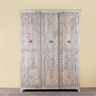 Large hand carved mango wood wardrobe with floral carvings, whitewashed finish, four doors, and drawer storage.
