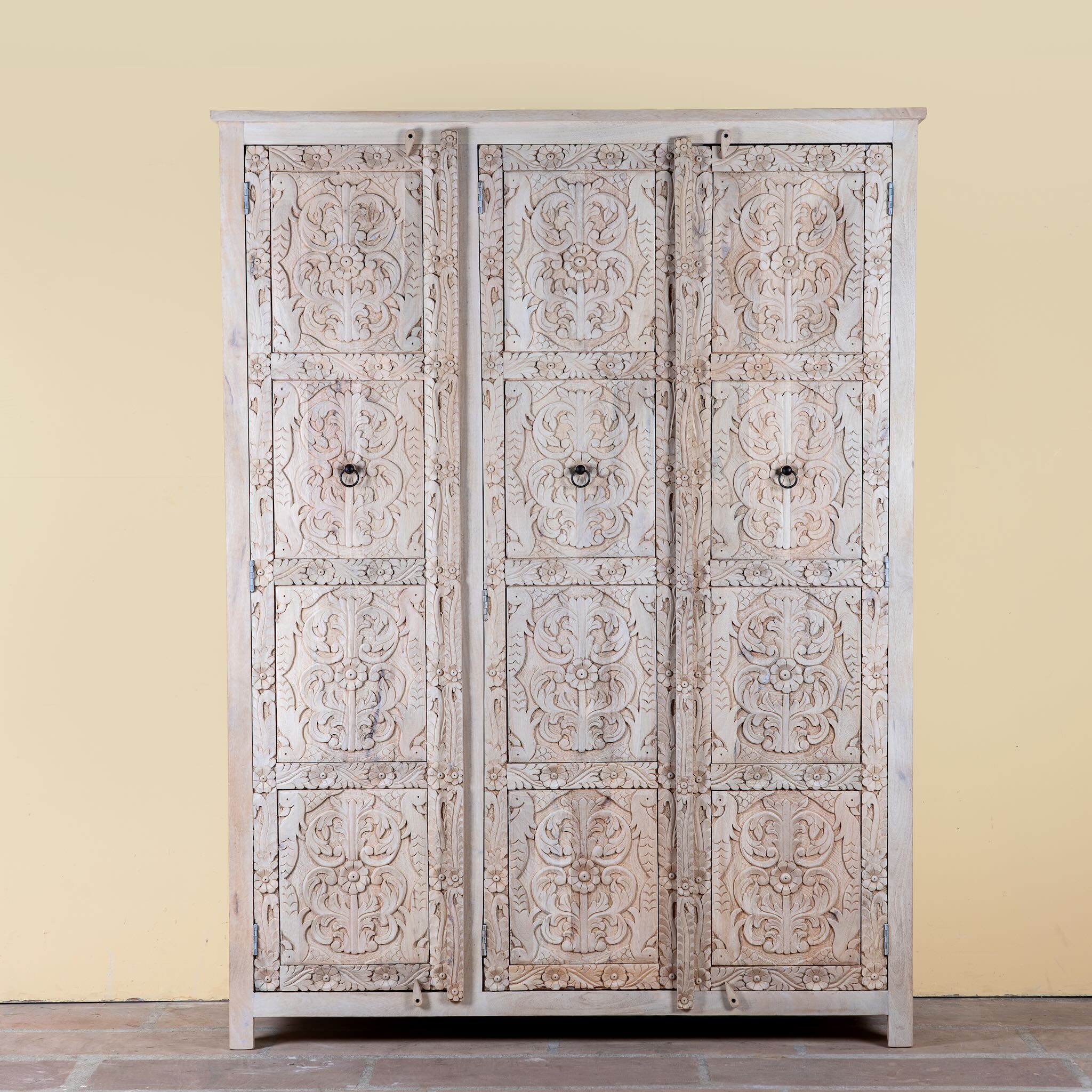 Large hand carved mango wood wardrobe with floral carvings, whitewashed finish, four doors, and drawer storage.