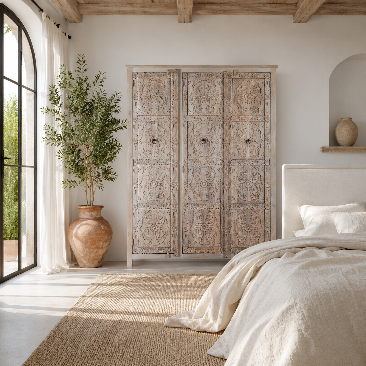 Lifestyle image of a large hand carved mango wood wardrobe with floral carvings, whitewashed finish, four doors, and drawer storage.