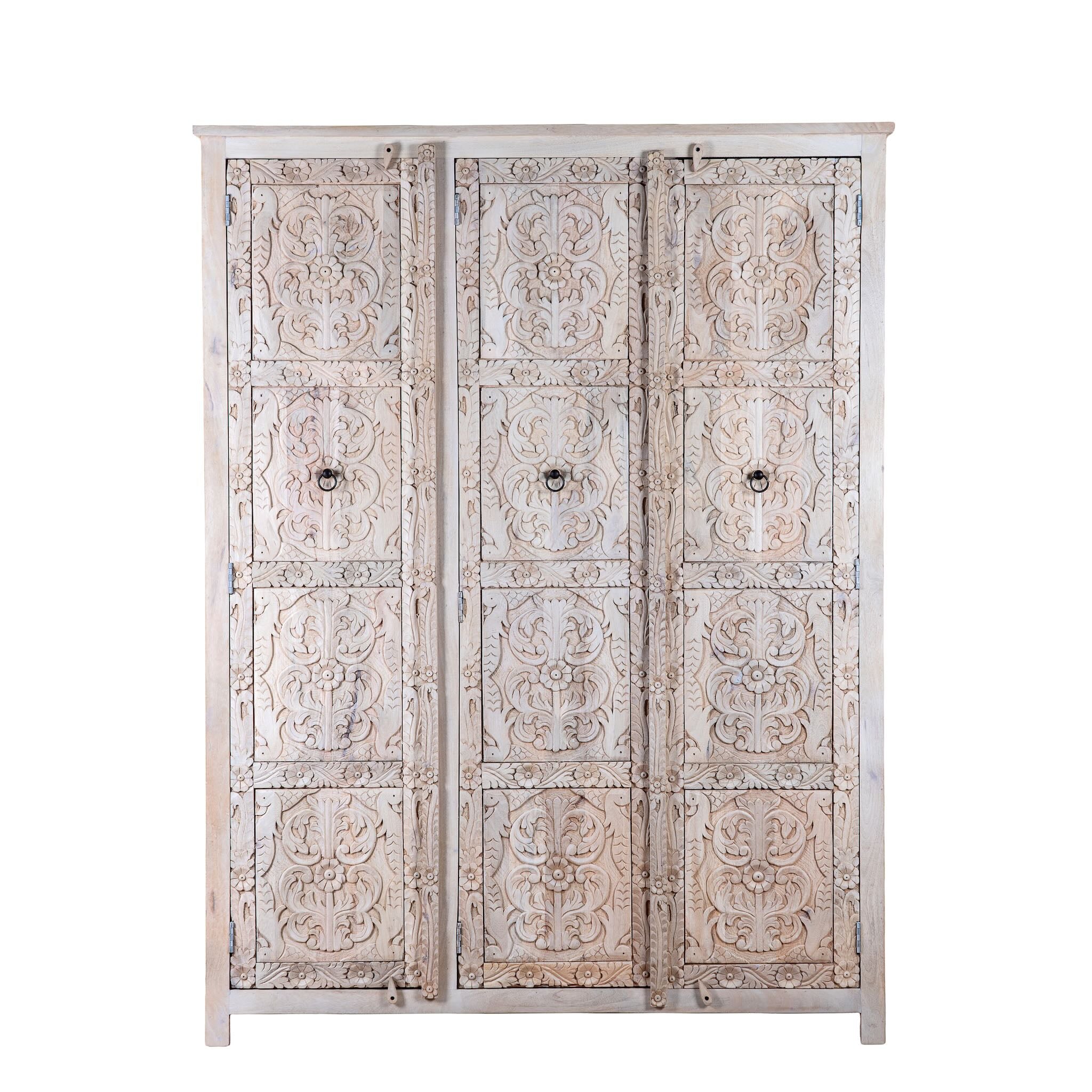 White background image of a large hand carved mango wood wardrobe with floral carvings, whitewashed finish, four doors, and drawer storage.