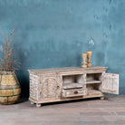 Side angle view of a carved mango wood lowboard with floral doors, crackled vintage finish, drawer, and open shelf, 150 × 40 × 64 cm.