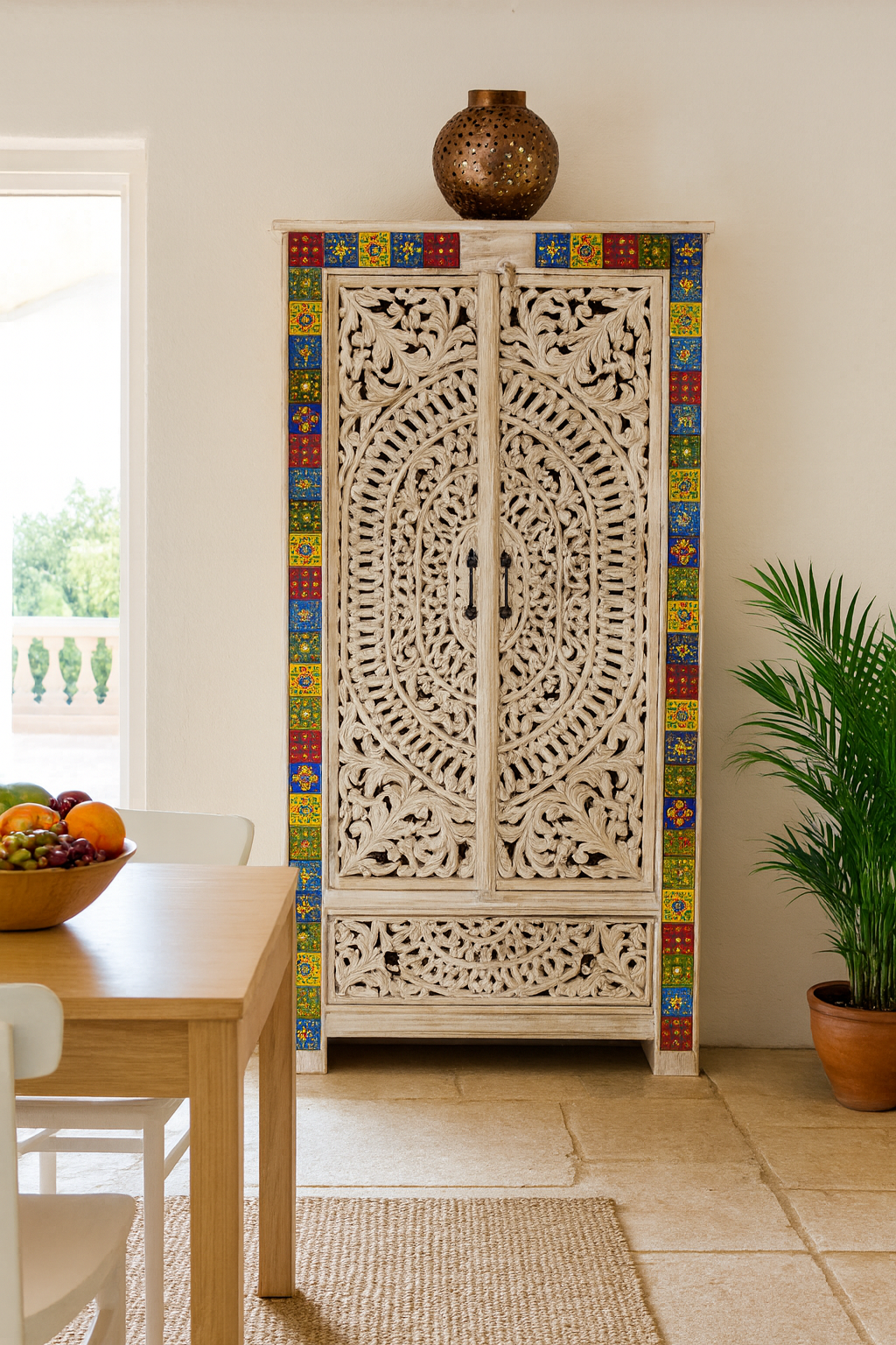 Decorative carved cabinet with colorful tile border in a room with a table and plants.