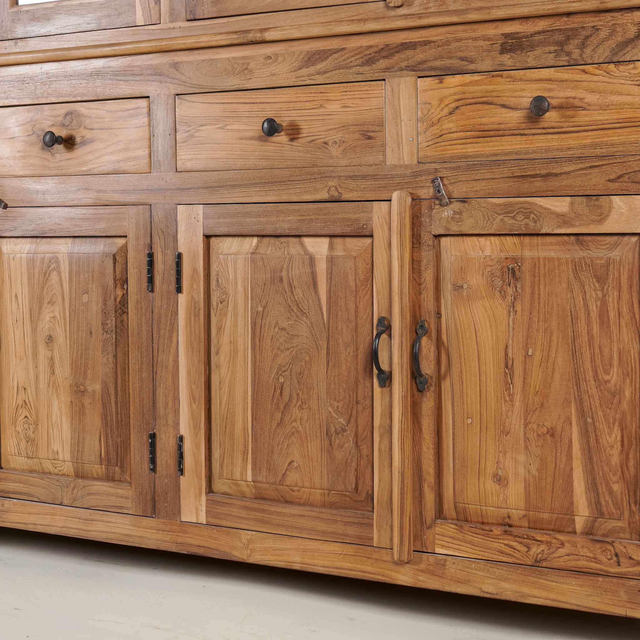 Close up image of a two-part showcase cabinet made from reclaimed teak wood, featuring glass-panel upper doors for display, four drawers for storage, and lower cabinets with solid wood doors in a natural finish.