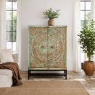 Lifestyle imagination of a carved mango wood cabinet with floral hand-carving, distressed green finish, iron stand, 100 × 40 × 150 cm.